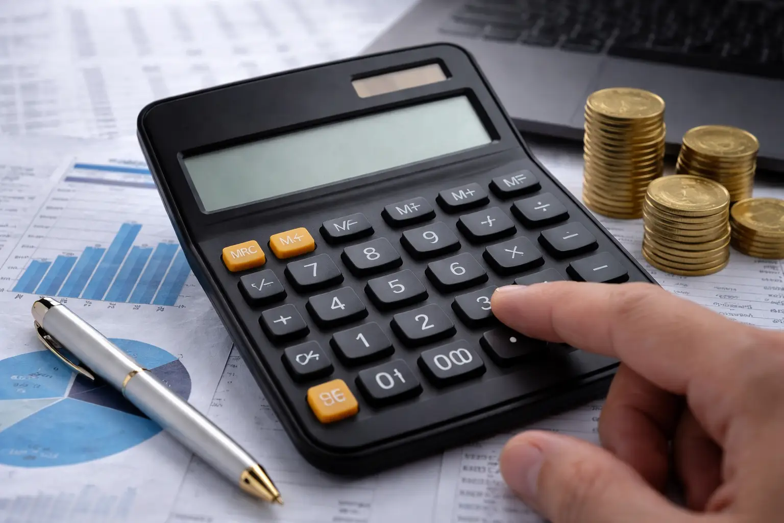 Calculator on financial reports with charts, coins, and a pen on a desk